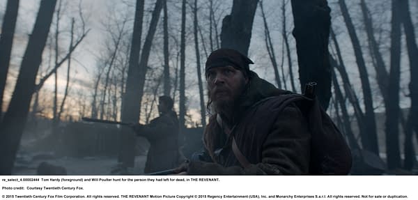 Tom Hardy and Will Poulter appear in a snowy, forested setting, focused on their hunt in a dramatic scene from the film THE REVENANT.