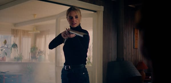 A still from 'Over Your Dead Body' featuring a woman in a black turtleneck, holding a shotgun, appearing assertive and on guard. The scene is set in a warmly lit room with indoor plants and a cozy ambiance.