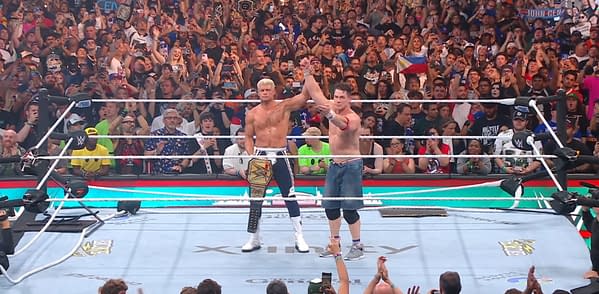 In a wrestling ring, John Cena raises Cody Rhodes' arm in victory after Rhodes defeats him for the WWE title at SummerSlam, while a cheering crowd watches in the background.