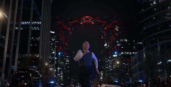 A scene from Disney's live-action TRON: ARES features Greta Lee as Kim running through a futuristic city at night, with illuminated buildings and a massive, glowing structure in the background.