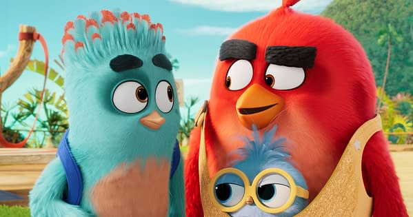 Red stands with his two sons in a colorful Angry Birds Movie 3 scene, with the younger chick in oversized yellow glasses.