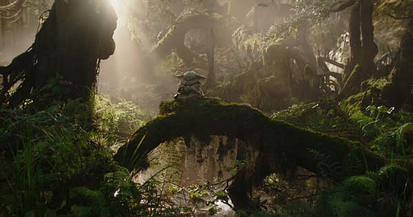 In a lush, green, misty forest, Grogu, a small, green creature from Lucasfilm's The Mandalorian, sits calmly on a mossy log, surrounded by vibrant foliage and dappled sunlight.