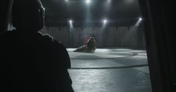 A scene from 'The Mandalorian' featuring the armored figure of the Mandalorian observing Rotta the Hutt in a dimly lit arena, highlighting the tension of their encounter.