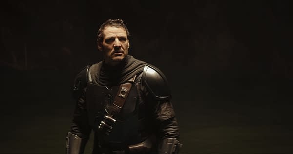 Pedro Pascal as the Mandalorian stands in dark armor against a shadowy background in The Mandalorian and Grogu.