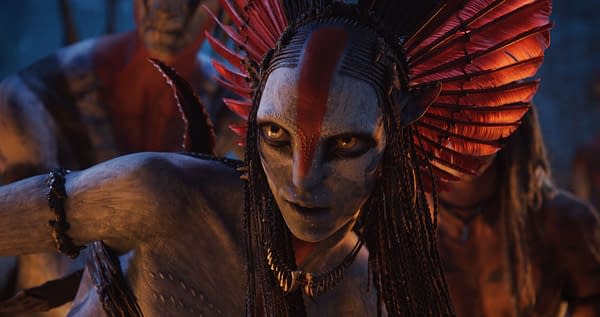 A character named Varang, portrayed by Oona Chaplin, features striking face paint and intricate accessories, set in a dramatic lighting typical of the 20th Century Studios' film 'Avatar: Fire and Ash.' The background includes shadowy figures, highlighting the character's fierce expression.