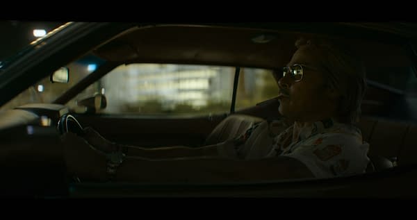 Brad Pitt as Cliff Booth drives at night in a dimly lit car, smoking a cigarette.