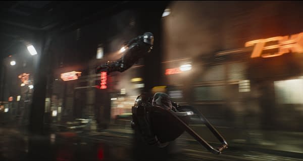 A scene from 'The Mandalorian and Grogu' shows a character in a sleek, armored suit soaring through a futuristic cityscape, while Grogu sits securely in a hovering pod. The atmosphere is dramatic, highlighted by glowing neon signs and a misty ambiance.