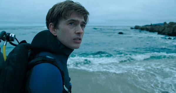 Austin Abrams as Jay Gardiner in Whalefall, wearing scuba gear and looking out over a rough ocean shoreline.