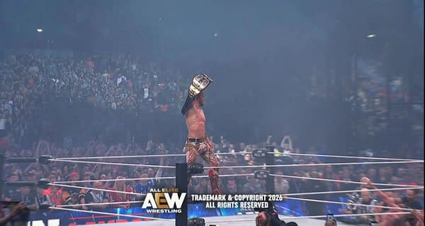 Will Ospreay stands in the AEW ring at Wembley Stadium, holding up the AEW Championship in front of a roaring crowd. Smoke hangs in the arena after his title win at AEW All In London.