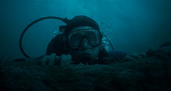 A scuba diver peers over the ocean floor in a dark underwater scene from Whalefall, with bubbles rising behind him.