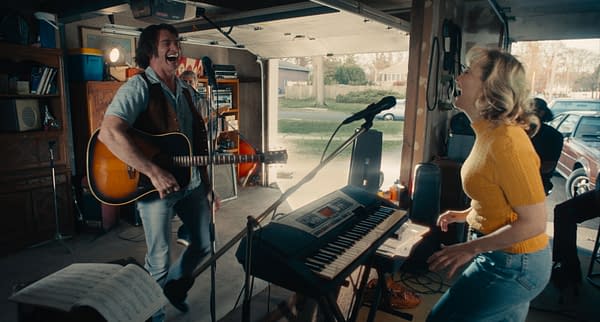 Hugh Jackman as Mike Sardina and Kate Hudson as Claire Stengl perform joyfully in a garage, with Jackman playing guitar and Hudson dancing, in the film 'Song Sung Blue'. The scene captures a lively musical moment filled with enthusiasm and connection.
