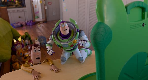 Woody, with a worried expression, clings to a table while Buzz Lightyear looks startled, both featured in a scene from Disney and Pixar's Toy Story 5. A green toy with a bunny ear design is visible in the foreground, set against a messy children's room.