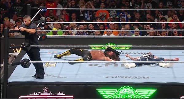 In the ring at WWE SummerSlam, two wrestlers lie on the mat, seemingly defeated after a match. A referee is nearby, appearing to manage the situation as a crowd watches intently.