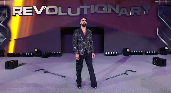 A wrestler wearing a sequined blazer, Seth Rollins, stands confidently in an arena, with a spotlight on him. The background features the word 'REVOLUTIONARY' prominently displayed. Rollins has just revealed he's was faking an injury.