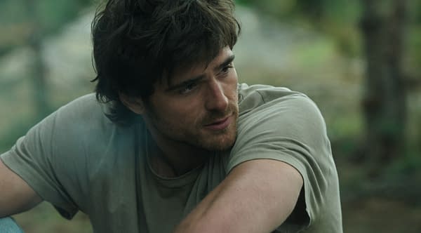 Jacob Elordi as Hig in The Dog Stars, leaning forward outdoors in a muted, forested setting.