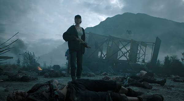 Margaret Qualley as Cima stands armed in a smoky, post-apocalyptic landscape surrounded by fallen bodies and wreckage in The Dog Stars.