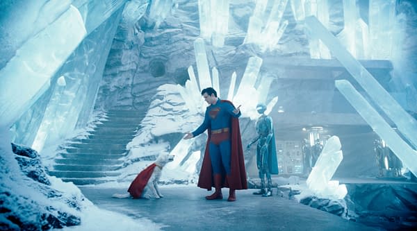 Superman stands in an icy, crystalline environment, interacting with a dog wearing a cape, while a humanoid robot observes nearby. The scene conveys a whimsical mix of superhero and science fiction elements.