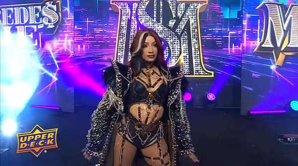 Mercedes Monè stands on the AEW Dynamite stage in an ornate black entrance outfit amid purple and blue lights.