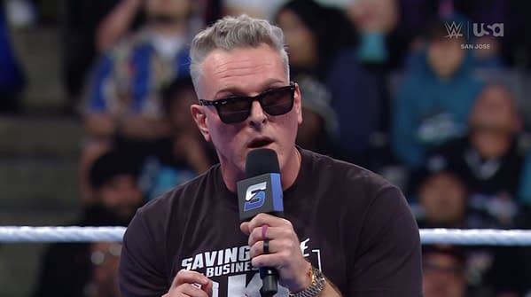 Pat McAfee speaks into a microphone while wearing sunglasses, standing in a wrestling ring. The audience is visible behind him, reacting to his taunts directed at the WWE Universe.