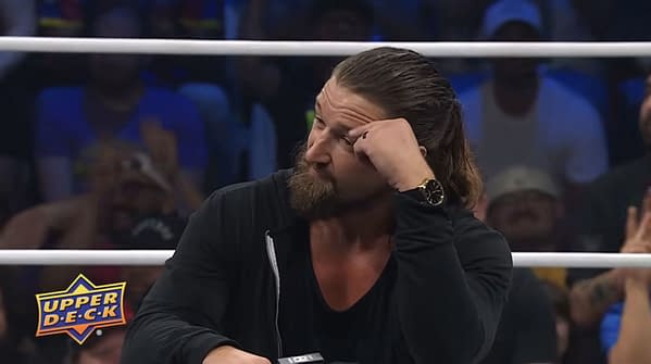 Jay White sits in the AEW ring with his hand to his temple, wearing a black jacket and watch, as the crowd looks on. The Upper Deck logo appears in the corner.