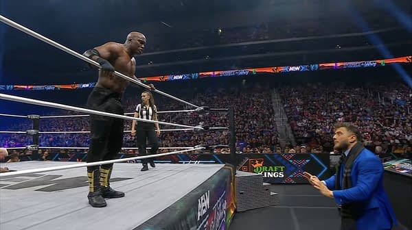 A tense moment at AEW Double or Nothing, featuring The Hurt Syndicate's Bobby Lashley, a wrestler in black attire standing next to the ropes, while another man in a blue suit, MJF, gestures toward him. The ring is surrounded by a cheering crowd and a referee watches attentively.