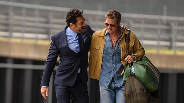 Two men walk closely together, one wearing a suit and tie and the other in a casual outfit with sunglasses, both appearing friendly in a setting likely related to Formula 1.