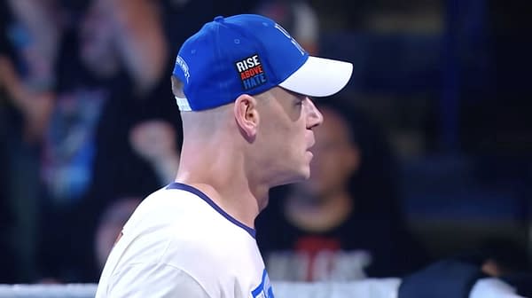 John Cena, wearing a blue and white cap with the words Rise Above Hate, appears in profile during a WWE SmackDown event, showcasing his determined expression and iconic look.