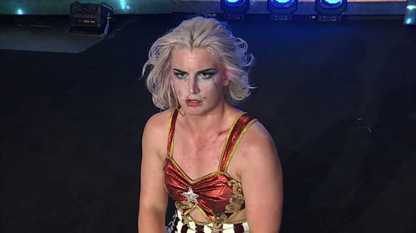 Toni Storm, in a red and gold costume, shows a surprised expression after Ronda Rousey's unexpected appearance at AEW Revolution, with faint makeup smudges on her face.