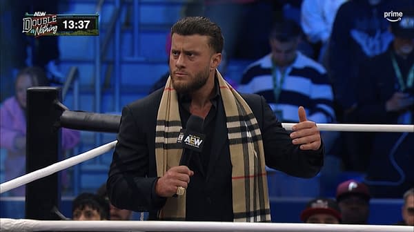 MJF stands in the AEW ring during the Double or Nothing Buy-In pre-show, speaking into a microphone with a stern expression. He wears a black suit and a beige plaid scarf.