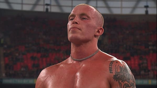 Kyle Fletcher stands shirtless in the ring at AEW All In London, wearing a chain necklace and showing a shoulder tattoo, with the arena crowd blurred behind him.