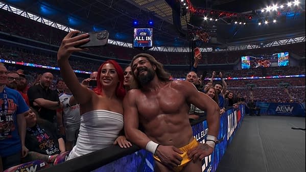 Andrade poses for a selfie with a fan ringside during the Casino Gauntlet match at AEW All In: London. The packed stadium and big arena screens frame the moment.