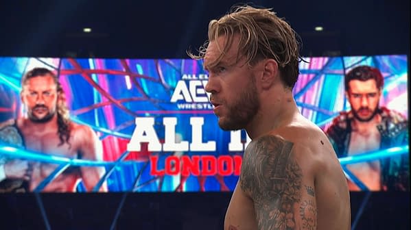 Will Ospreay stands in profile inside an AEW arena, with an All In London matchup graphic glowing on the screen behind him.