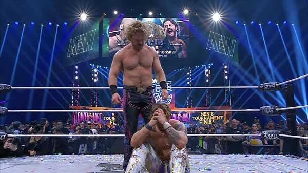 Hangman Adam Page stands triumphantly over a kneeling Will Ospreay in a wrestling ring, celebrating his victory. Confetti is scattered on the canvas, with colorful lights illuminating the arena in the background.