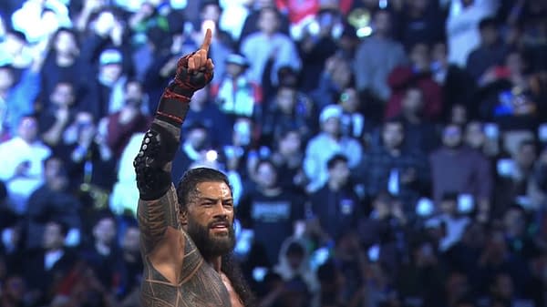 A jubilant Roman Reigns raises his arm in victory after winning the Royal Rumble match, surrounded by a cheering crowd in Saudi Arabia.