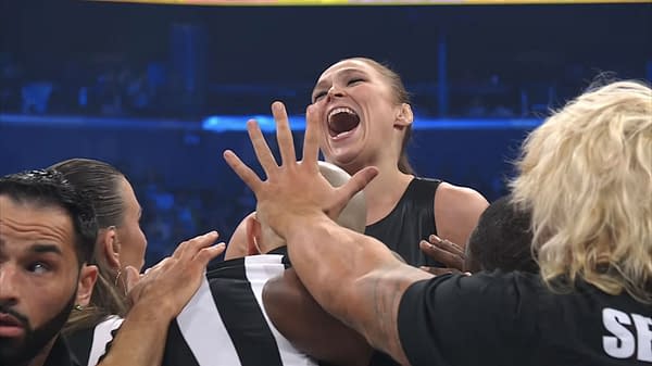 Ronda Rousey laughing and being held back by officials during an AEW Revolution event. The scene captures her excitement as she challenges Toni Storm.