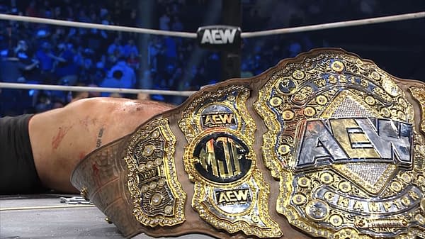 The AEW Men's World Championship belt lies on the ground, stained with blood, symbolizing the extreme violence associated with recent wrestling events. The belt features intricate golden detailing and the AEW logo prominently displayed.