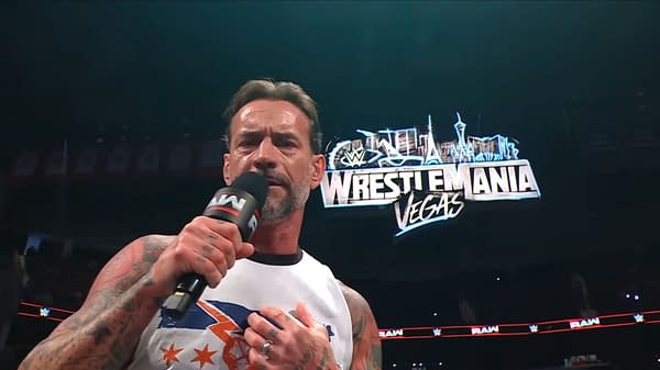 CM Punk addresses the fans while holding a microphone, with the WrestleMania Vegas sign visible in the background. The setting is a wrestling arena during WWE Raw.
