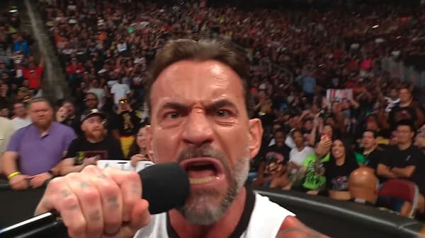 A man with a microphone passionately delivers a speech, showcasing intense emotions with a focused expression. A crowd of enthusiastic fans surrounds him, reacting with excitement in a vibrant arena.