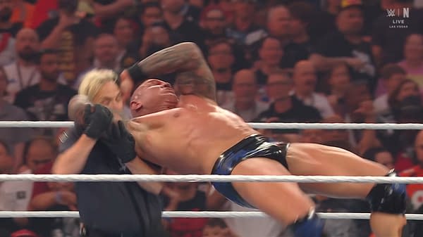A professional wrestler performs an RKO maneuver, aggressively attacking an opponent in a wrestling ring filled with fans. The intensity of the match is palpable.
