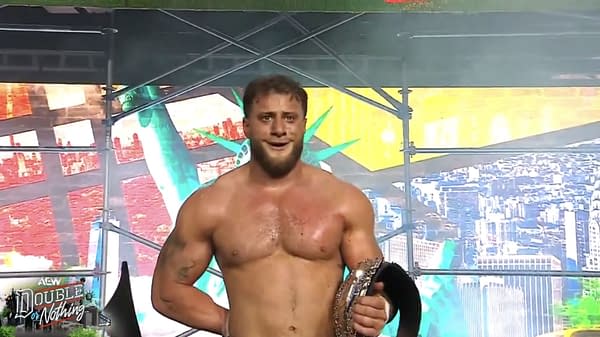 A shirtless wrestler smiles while holding a championship belt in front of an AEW Double or Nothing backdrop. The scene suggests MJF is pleased with the results of the event.