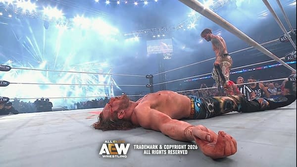 Will Ospreay stands over a defeated Kenny Omega in the AEW ring as bright lights fill the arena. Omega lies motionless after the championship match.