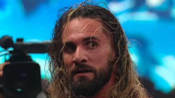 A close-up of Seth Rollins, a professional wrestler with long hair and a beard, looking intensely while a camera is focused on him during WWE SmackDown. The image captures the dramatic atmosphere of a post-show brawl.