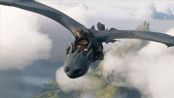 A character from 'How To Train Your Dragon' is riding on the back of a large, black dragon soaring above clouds and a coastline, capturing a sense of adventure and freedom.