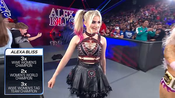 WWE superstar Alexa Bliss makes a stunning appearance during SmackDown, showcasing her signature edgy attire with pink highlights in her hair. A large crowd can be seen in the background, displaying excitement.