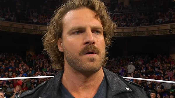 Hangman Adam Page, a professional wrestler, appears on stage at AEW Dynamite, displaying a serious expression with a crowd in the background.