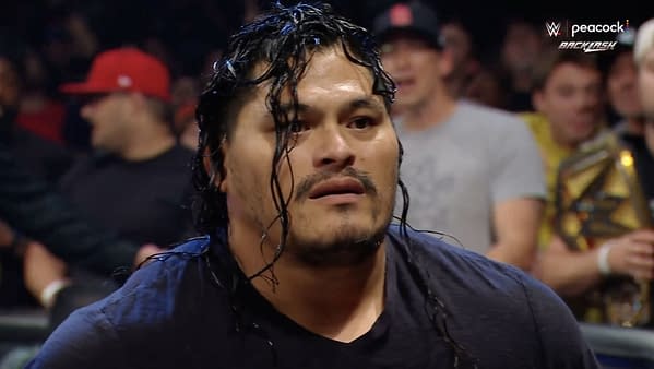 A man with long, wet hair has a shocked expression, surrounded by a lively crowd during a wrestling event. It is Jeff Cobb, making his debut at WWE Backlash.