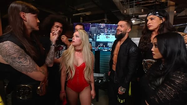A group of wrestlers from the Judgment Day faction on WWE Raw, showing various expressions of tension and disagreement among them. The setting is backstage, with a wrestling event visible on a monitor in the background.