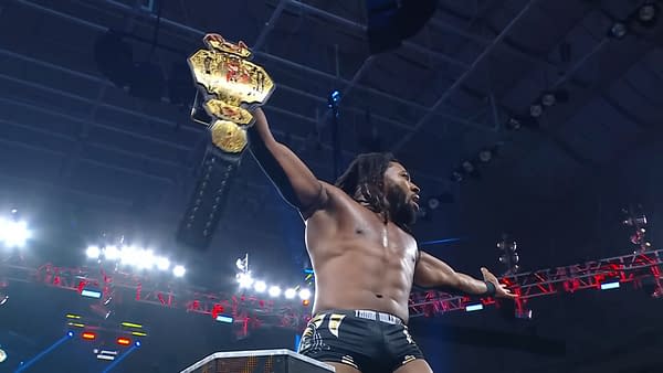 Trick Williams, celebrating his victory, holds the TNA Championship high above his head in a wrestling ring, with bright lights and a cheering crowd in the background.