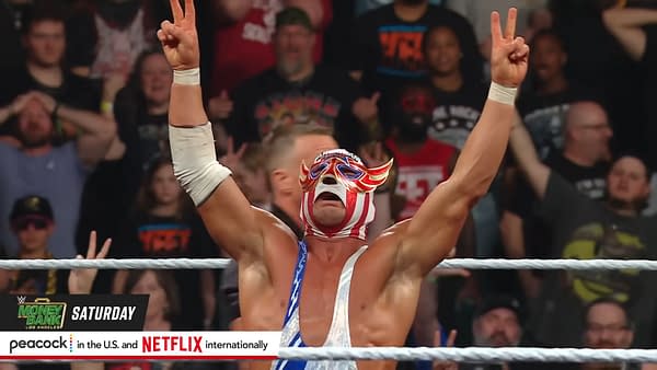 El Grande Americano, wearing a colorful mask and outfit, celebrates a victory in the wrestling ring, raising his arms in triumph. The excited crowd is visible in the background, reacting to the moment.
