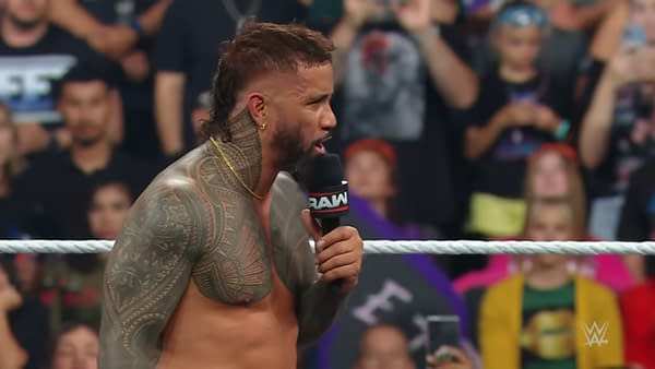 Jey Uso, a professional wrestler, delivers a passionate promo from the ring after losing the title to Gunther on WWE Raw, with a crowd of fans in the background. His muscular build and intricate tattoos are prominently displayed as he holds a microphone.